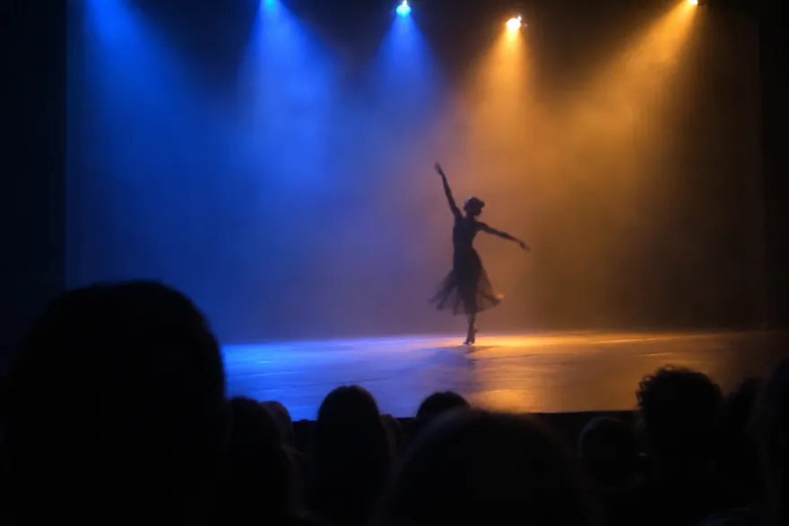 A dancer in silhouette on a stage lit in blue and amber, seen over the heads of the audience.