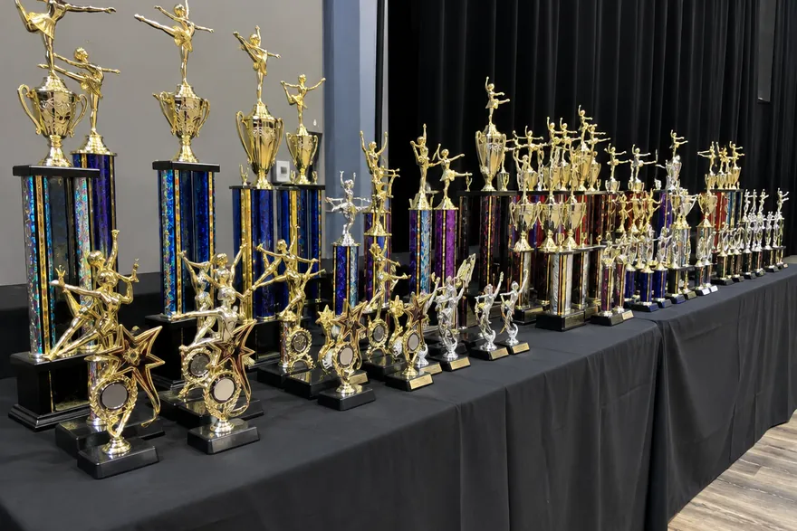 A long table beside a stage, lined with gold dance trophies of different heights.